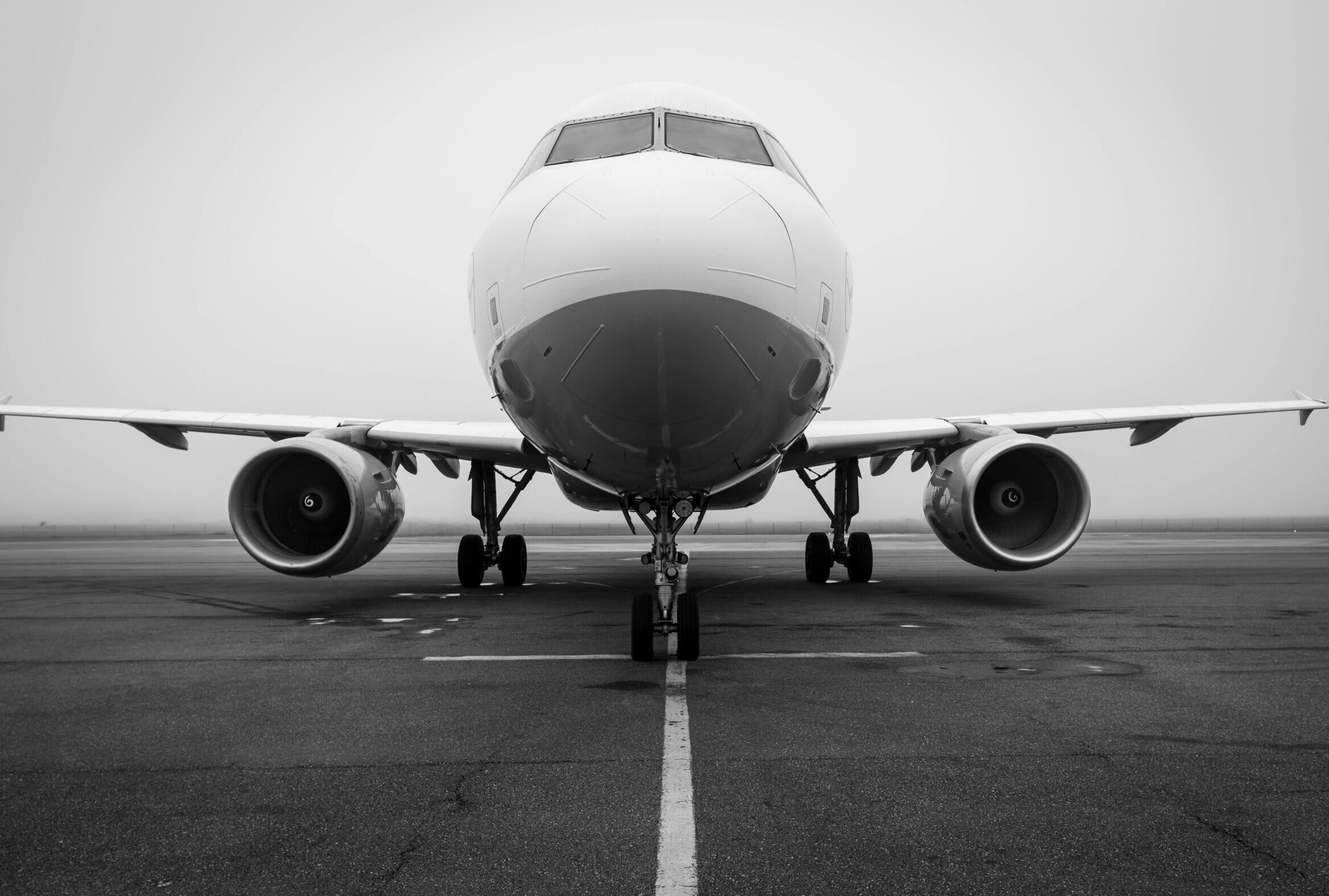 A black and white photo of an airplane on a foggy runway, captured head-on. Ideal for aviation themes.